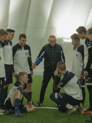 A soccer coach gives tactical advice to a youth team indoors on artificial turf.