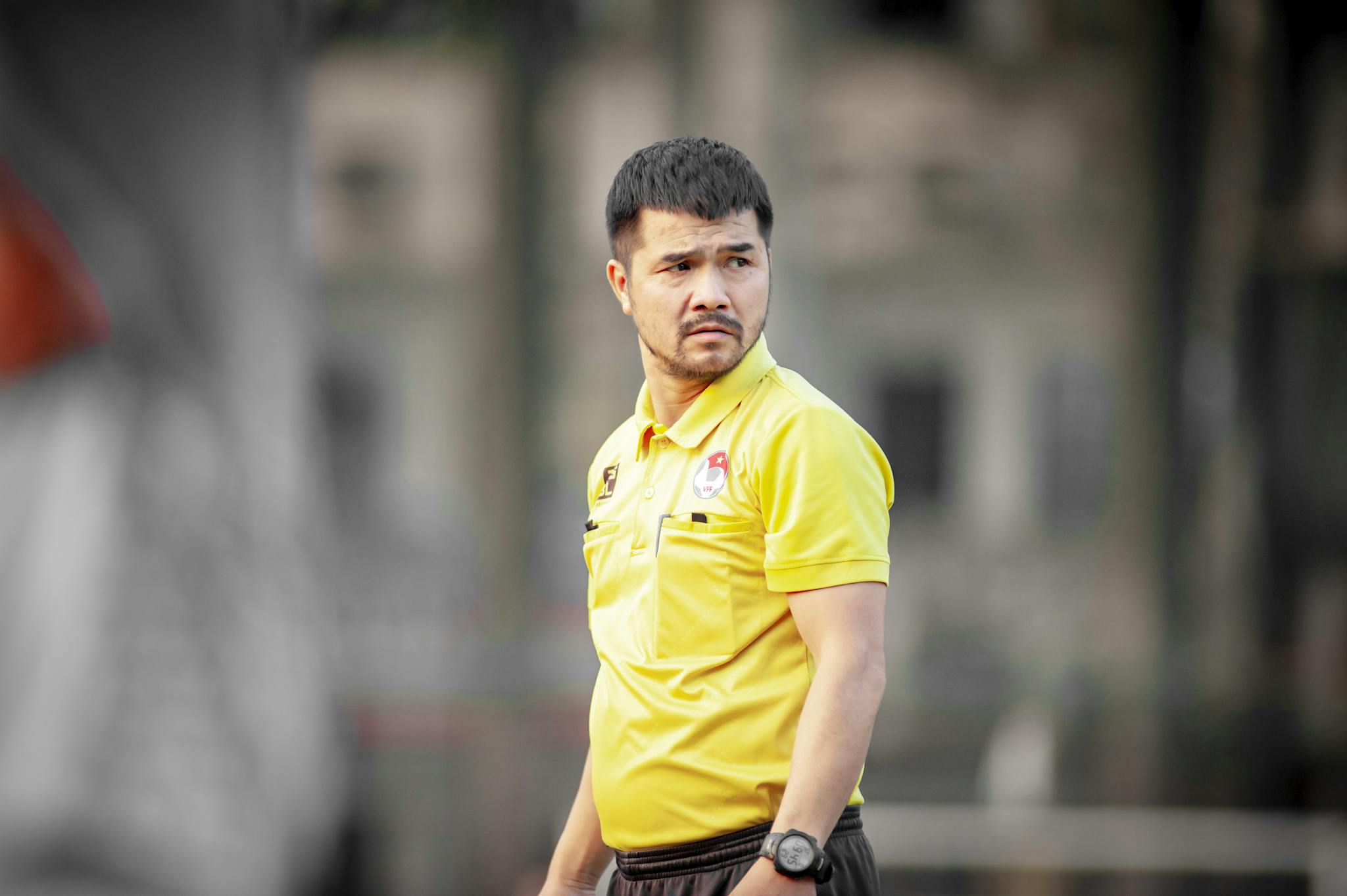 Focused soccer coach wearing yellow shirt during outdoor training session in Hanoi, Vietnam.